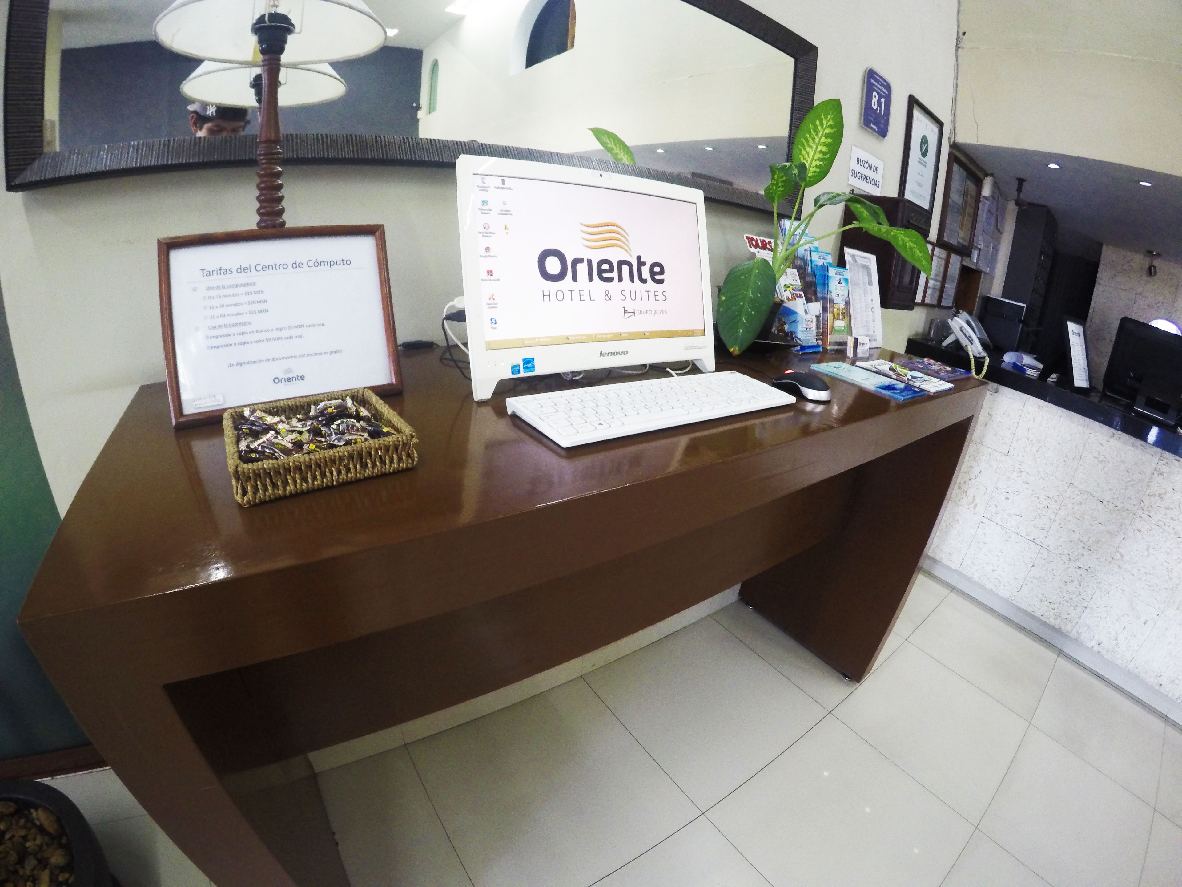 A hotel reception desk with a computer, a framed document, and a plant.