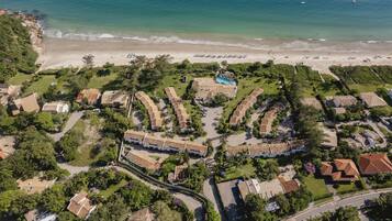 Vista aérea de un complejo turístico costero con playa, piscina y varias villas.
