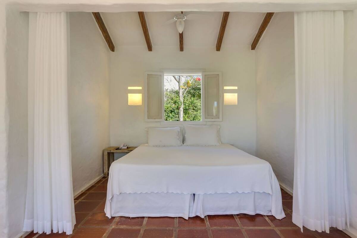 Une chambre à coucher avec un lit, des rideaux blancs, une fenêtre donnant sur un paysage agréable et des lampes fixées au mur.
