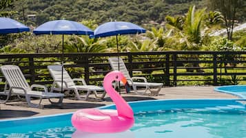 Relax by the pool surrounded by lush greenery and comfortable lounge chairs under shaded umbrellas.