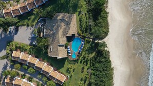 Vue aérienne d’un complexe hôtelier comprenant plusieurs bâtiments de style bungalow, une piscine et une plage.