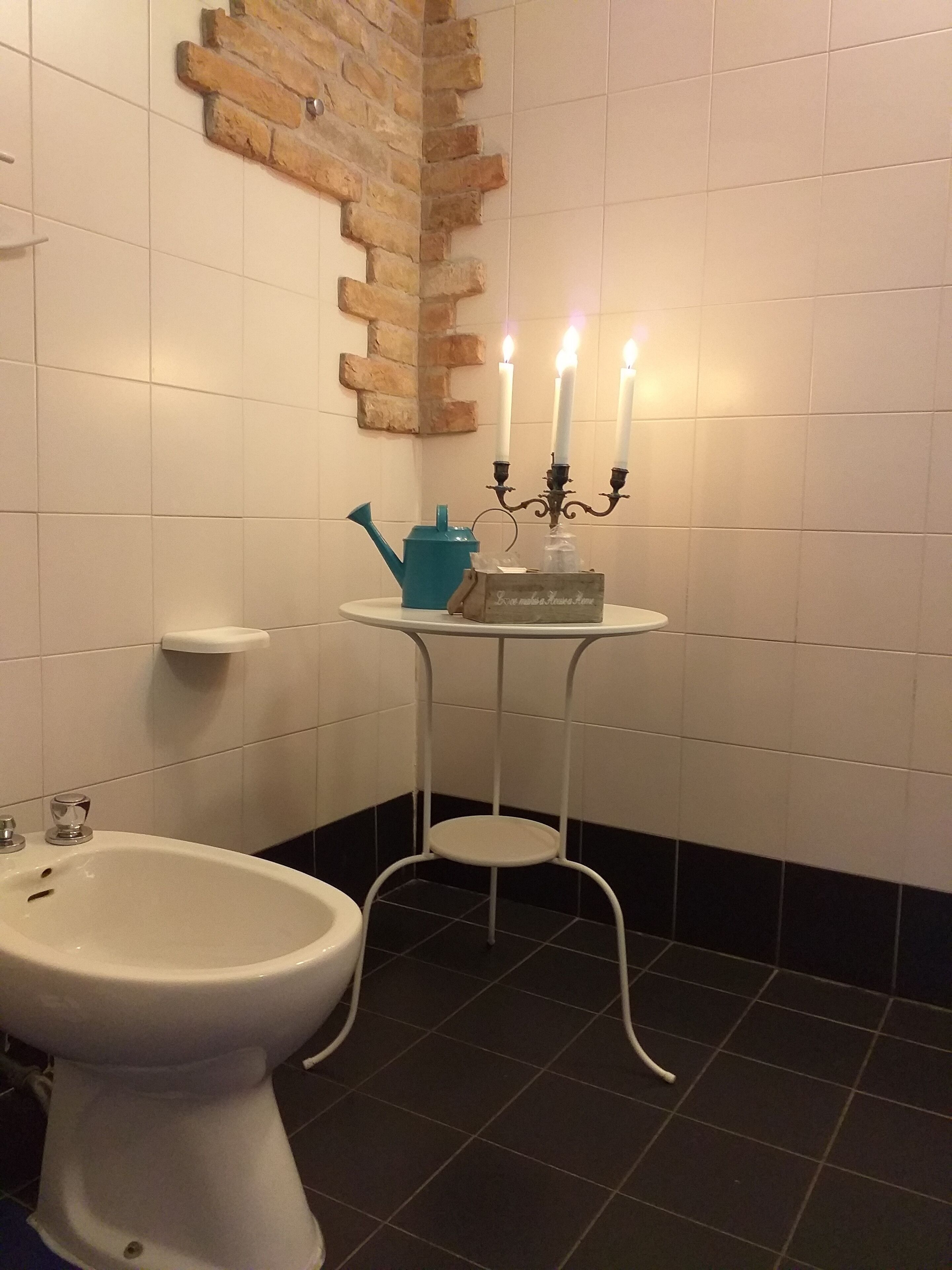 Ein Badezimmer mit Toilette, Bidet, einem kleinen Tisch mit einem Kandelaber und einer Kerze, sowie einer dekorativen Ziegelwand.