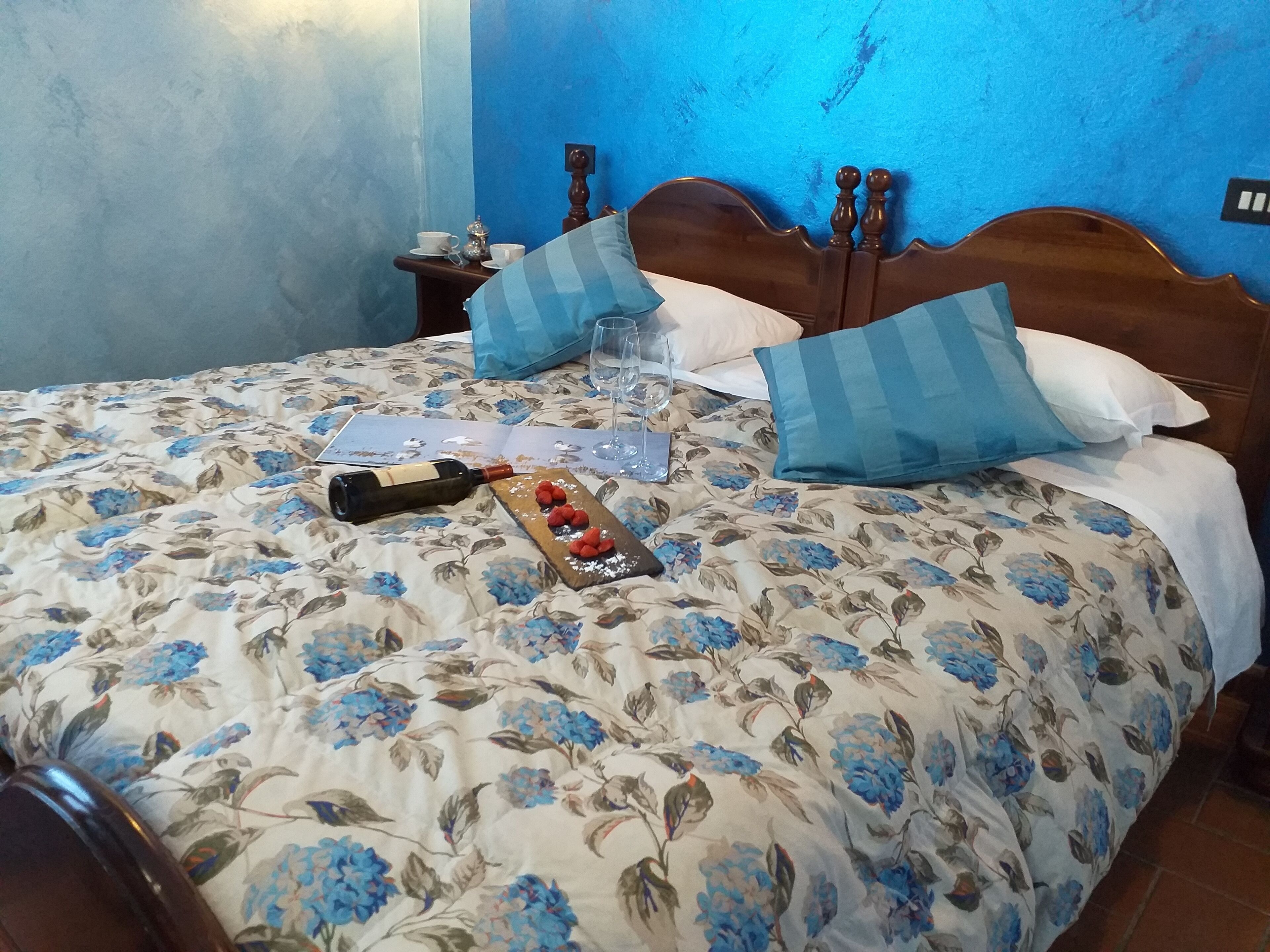 A bed with a floral bedspread, a wine bottle, and a tray with fruit on a table beside it.