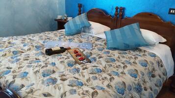 A bed with a floral bedspread, a wine bottle, and a tray with fruit on a table beside it.