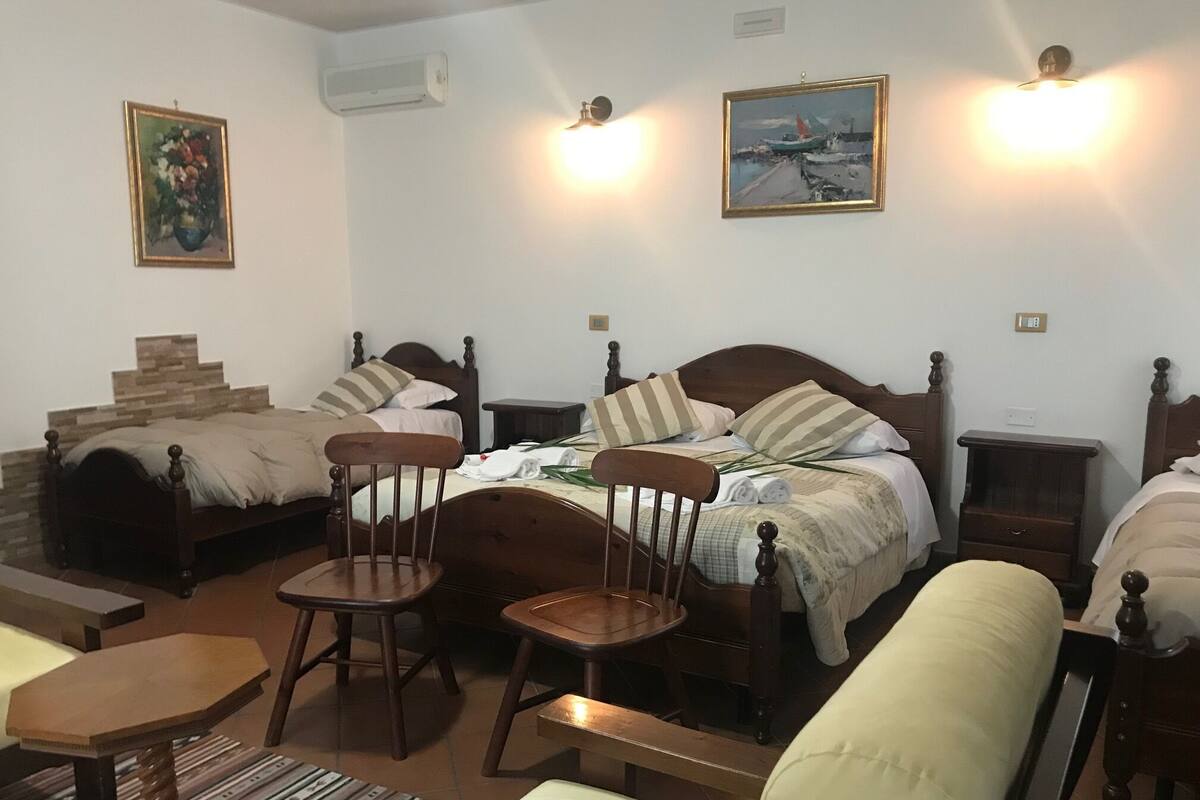 A bedroom with a large bed, two smaller beds, a wooden chair, a small table, and two wall-mounted lights.