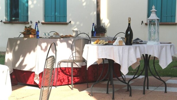 An outdoor dining area with a table set for two, featuring a bottle of wine, a lantern, and various food items.