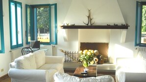 Una sala de estar con chimenea, sofás blancos, una mesa de centro y un portátil en una silla.