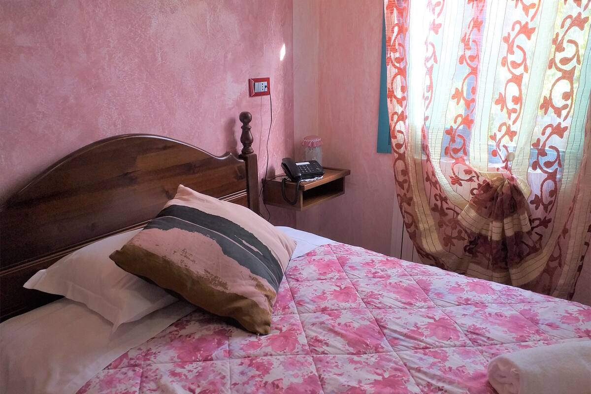 A bed with a floral bedspread, a wooden headboard, and a bedside table with a telephone and a small shelf.