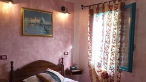 A bedroom with a wooden bed, pink walls, a painting, a nightstand, and a window with patterned curtains.