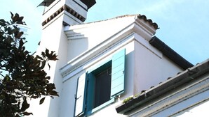 A building with a white facade, a black roof, and a window with blue shutters.