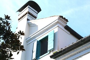 A building with a white facade, a black roof, and a window with blue shutters.