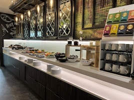 Montaje de bufé con diferentes alimentos y aderezos, una estación de café y una pared con un mural de un bosque.