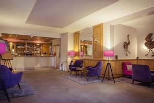 Vestíbulo de hotel con zona de bar, asientos morados y paneles de madera.
