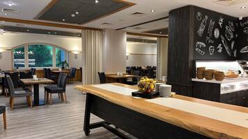 A modern restaurant interior with wooden tables, black chairs, and a chalkboard menu.