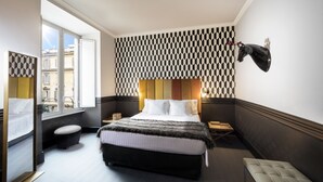 A hotel room with a large bed, a bench, a small table, a mirror, and a window with a view of buildings. - Manfredi Luxury Apartments (Rome)