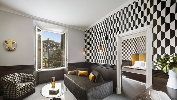A modern hotel room with a geometric patterned wall, a sofa, a small round table, and a view of the outdoors. - Manfredi Luxury Apartments (Rome)