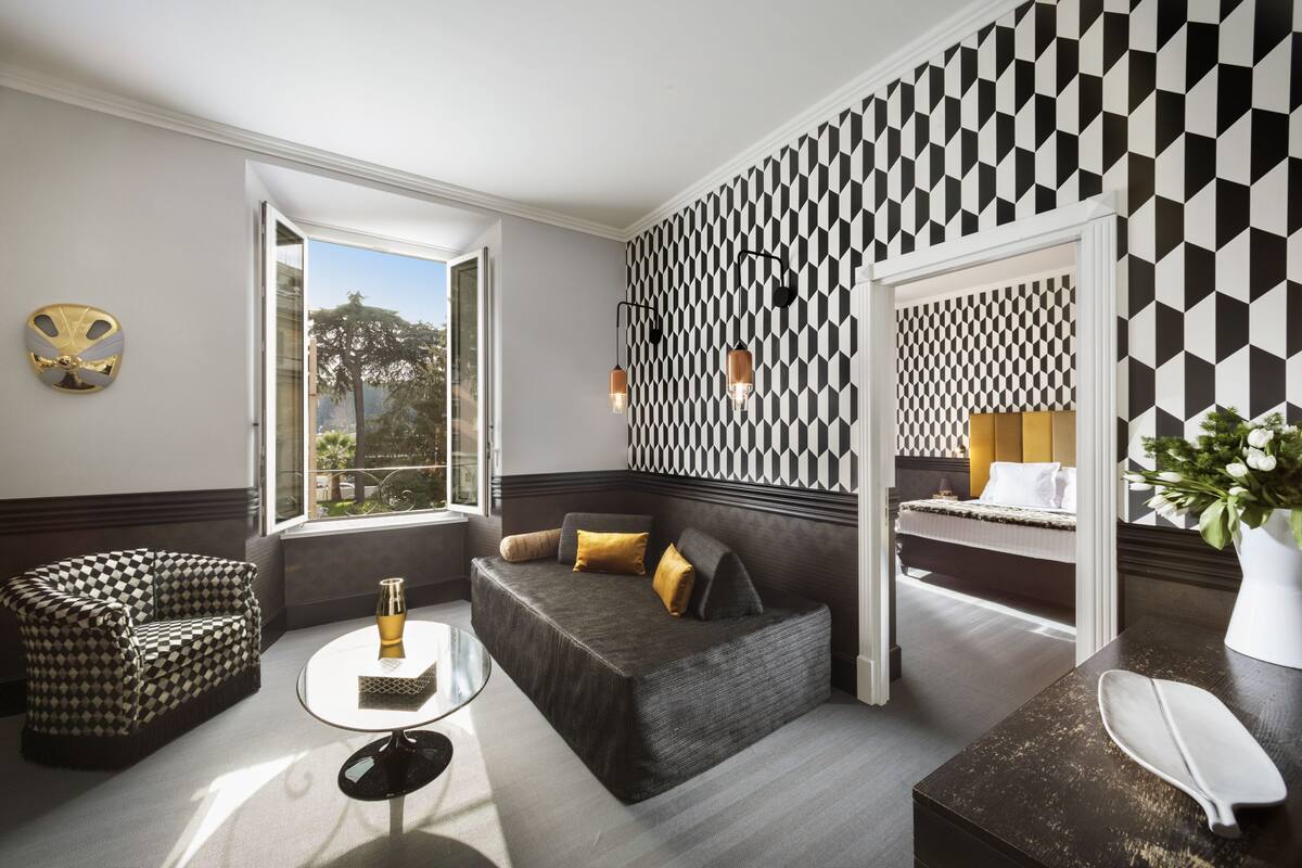 A modern hotel room with a geometric patterned wall, a sofa, a small round table, and a view of the outdoors.