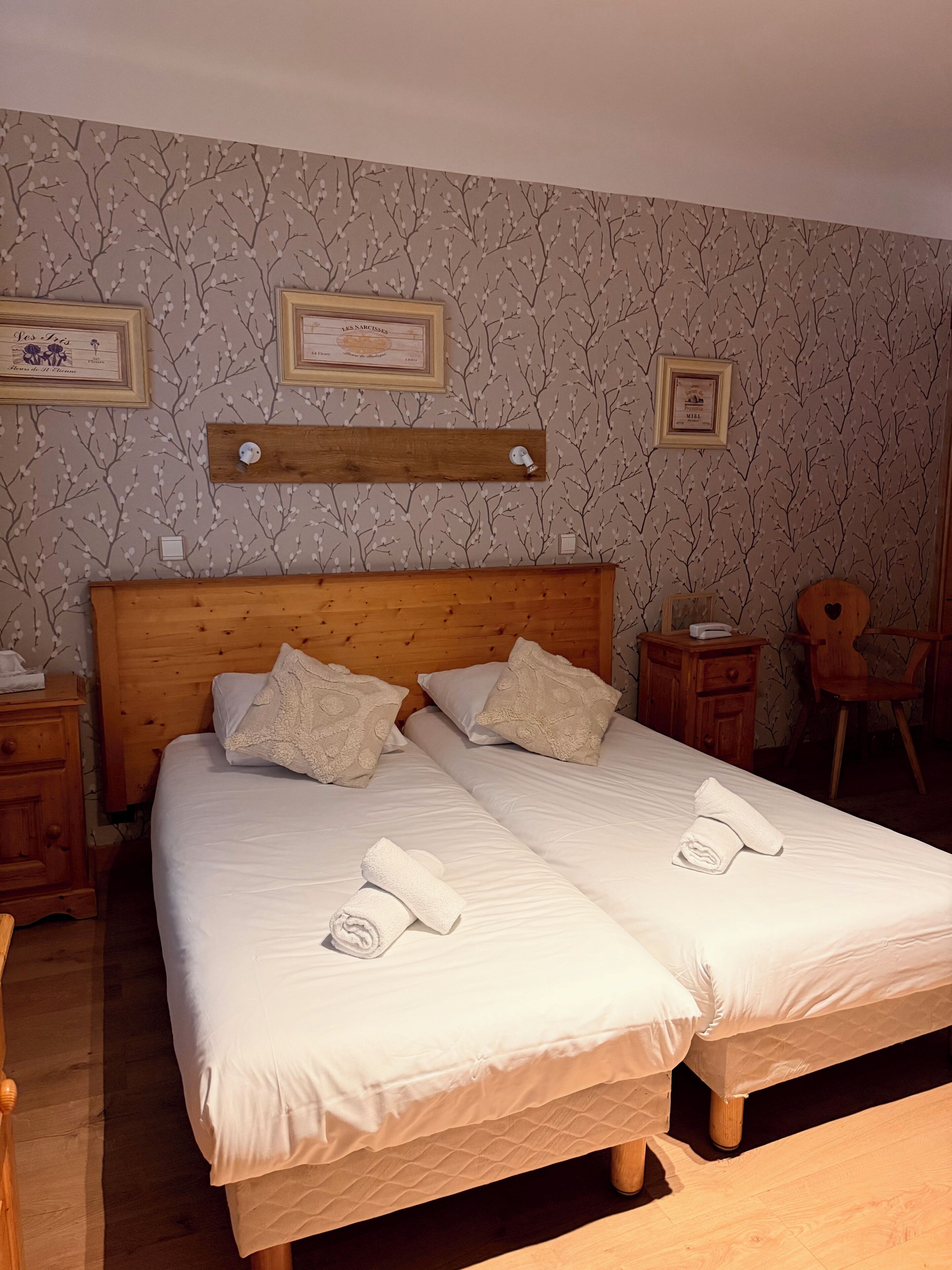 Una cama doble con sábanas blancas, dos almohadas y toallas enrolladas sobre un cabecero de madera.