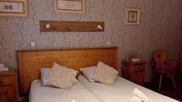 Una cama doble con sábanas blancas, dos almohadas y toallas enrolladas sobre un cabecero de madera.