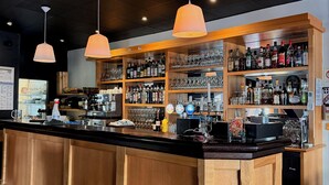 Un bar con armarios de madera, estantes con botellas, vasos y una barra.
