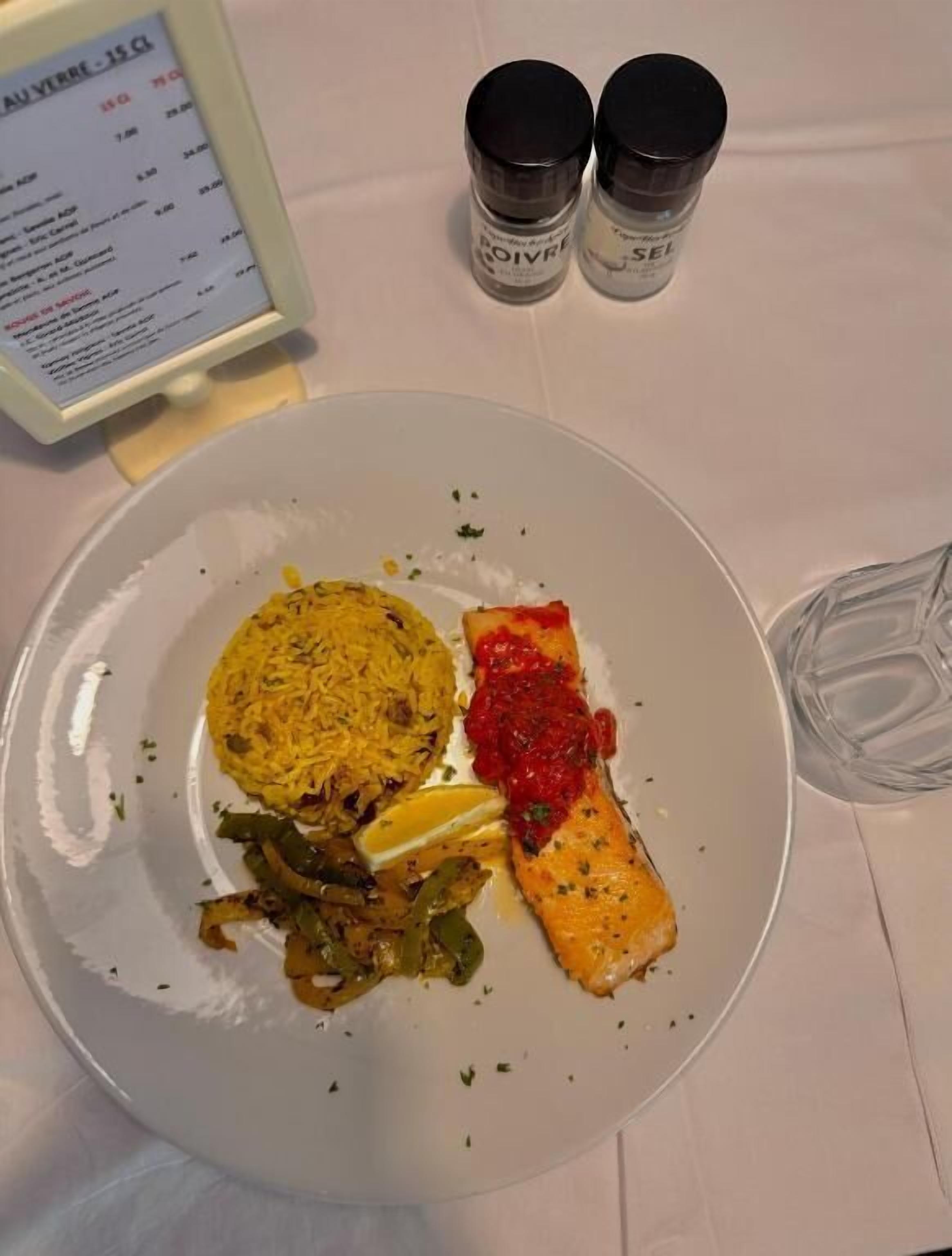 A plate with rice, salmon, and vegetables, a menu, and salt and pepper shakers on a table.