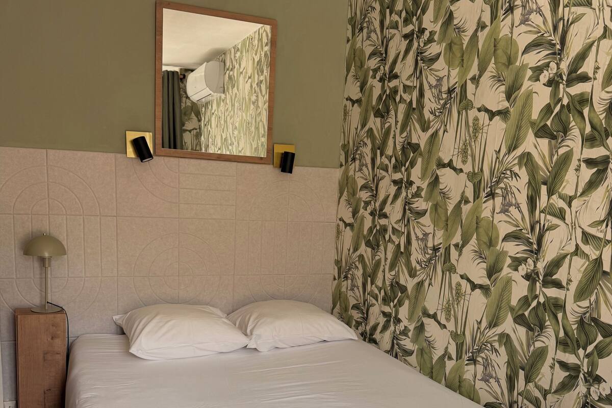 Une chambre d’hôtel avec un lit, un miroir, une lampe et un papier peint à motifs floraux.