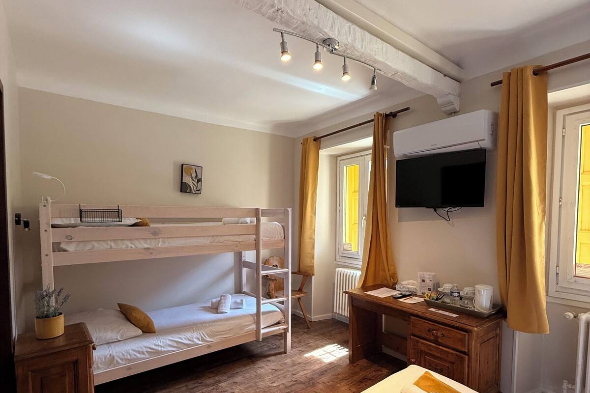 Une chambre avec des lits superposés, un bureau avec une chaise, une télévision et une fenêtre avec des rideaux.