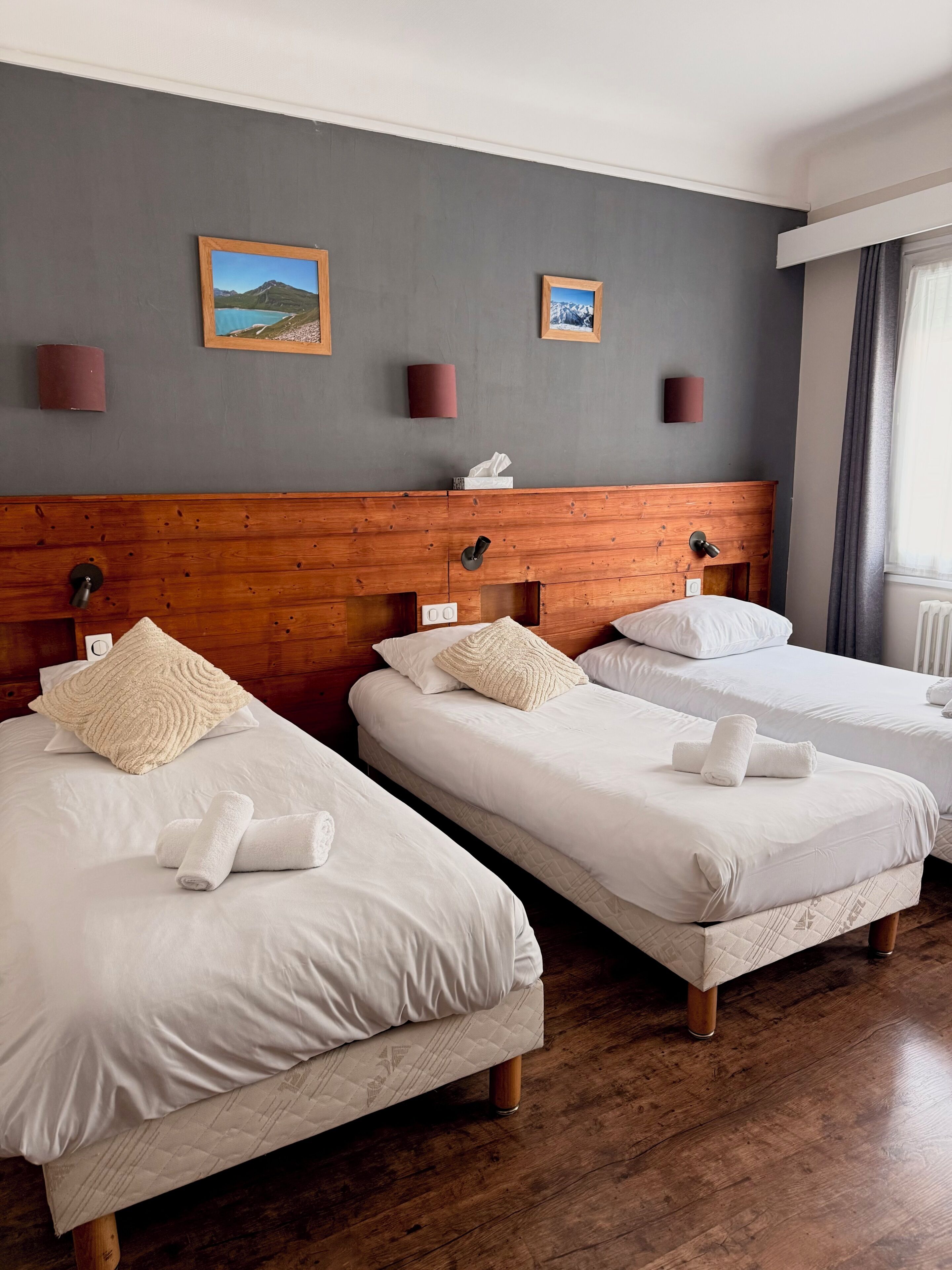 A hotel room with three single beds, wooden headboards, white bedding, and two framed pictures on the wall.