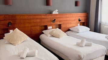 A hotel room with three single beds, wooden headboards, white bedding, and two framed pictures on the wall.