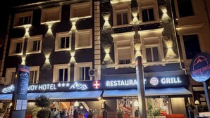 Hotel con restaurante y parrilla en la planta baja, con fachada moderna y ventanas iluminadas, y un letrero.