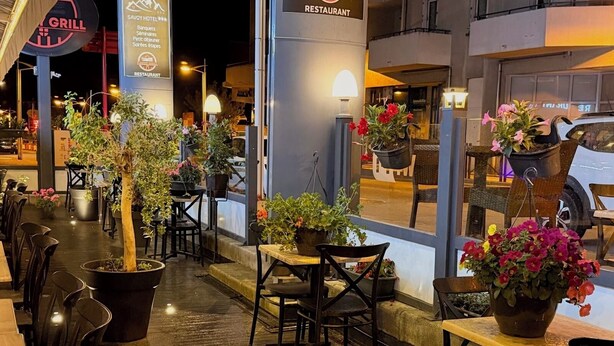 Un área de comedor al aire libre con mesas y sillas, plantas en macetas y un letrero para restaurante.