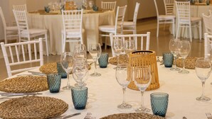 A dining area with round tables set with white chairs, blue glassware, and woven placemats. - Hotel Philadelfia (Peligros)