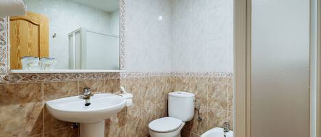Un baño con lavamanos, inodoro y bidé, con azulejos de mármol y un armario de madera.