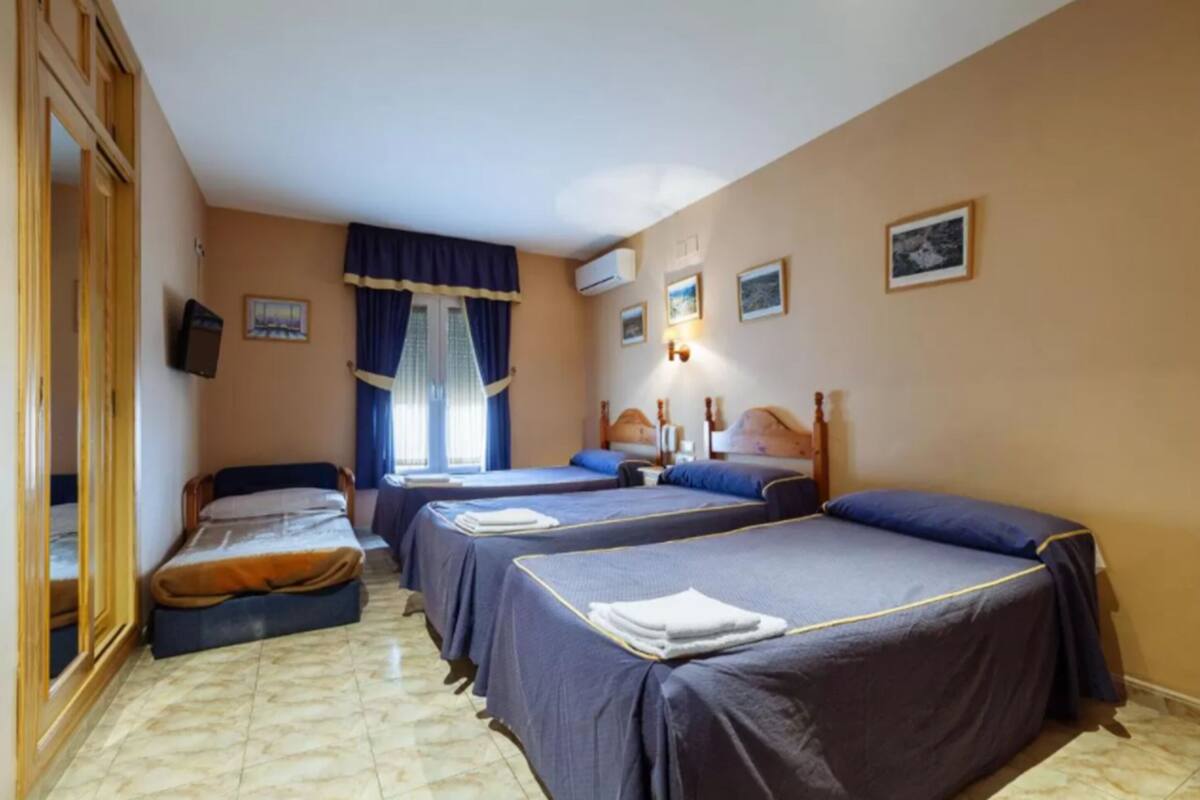 Ein Hotelzimmer mit zwei Einzelbetten, einem großen Spiegel, einem Kleiderschrank und einem Fenster mit Vorhängen.