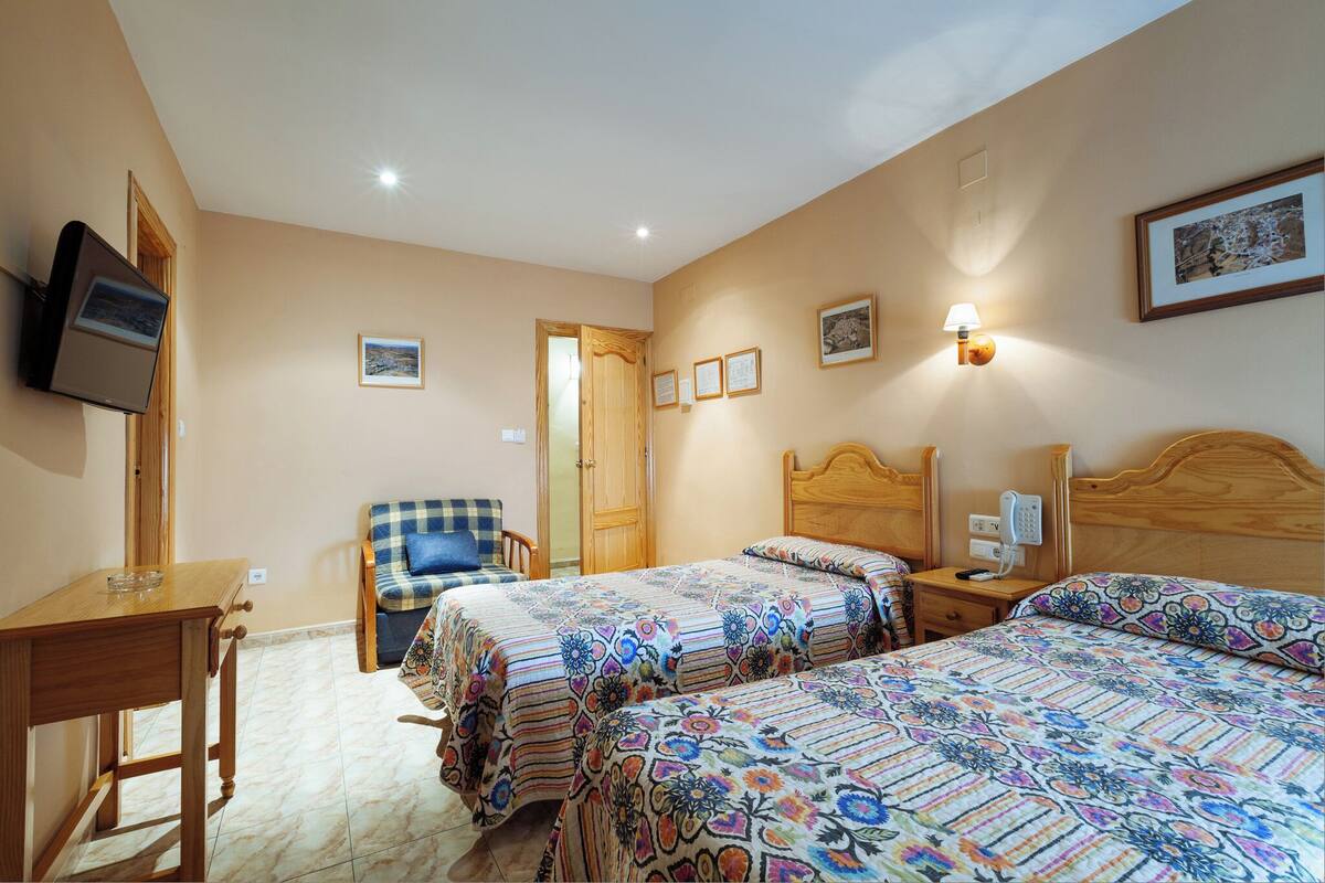 Ein Schlafzimmer mit zwei Betten, einem Holztisch, einem Stuhl und einem Fernseher an der Wand.