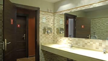 A hotel bathroom with a large mirror, two sinks, and a door with a red emergency exit sign.