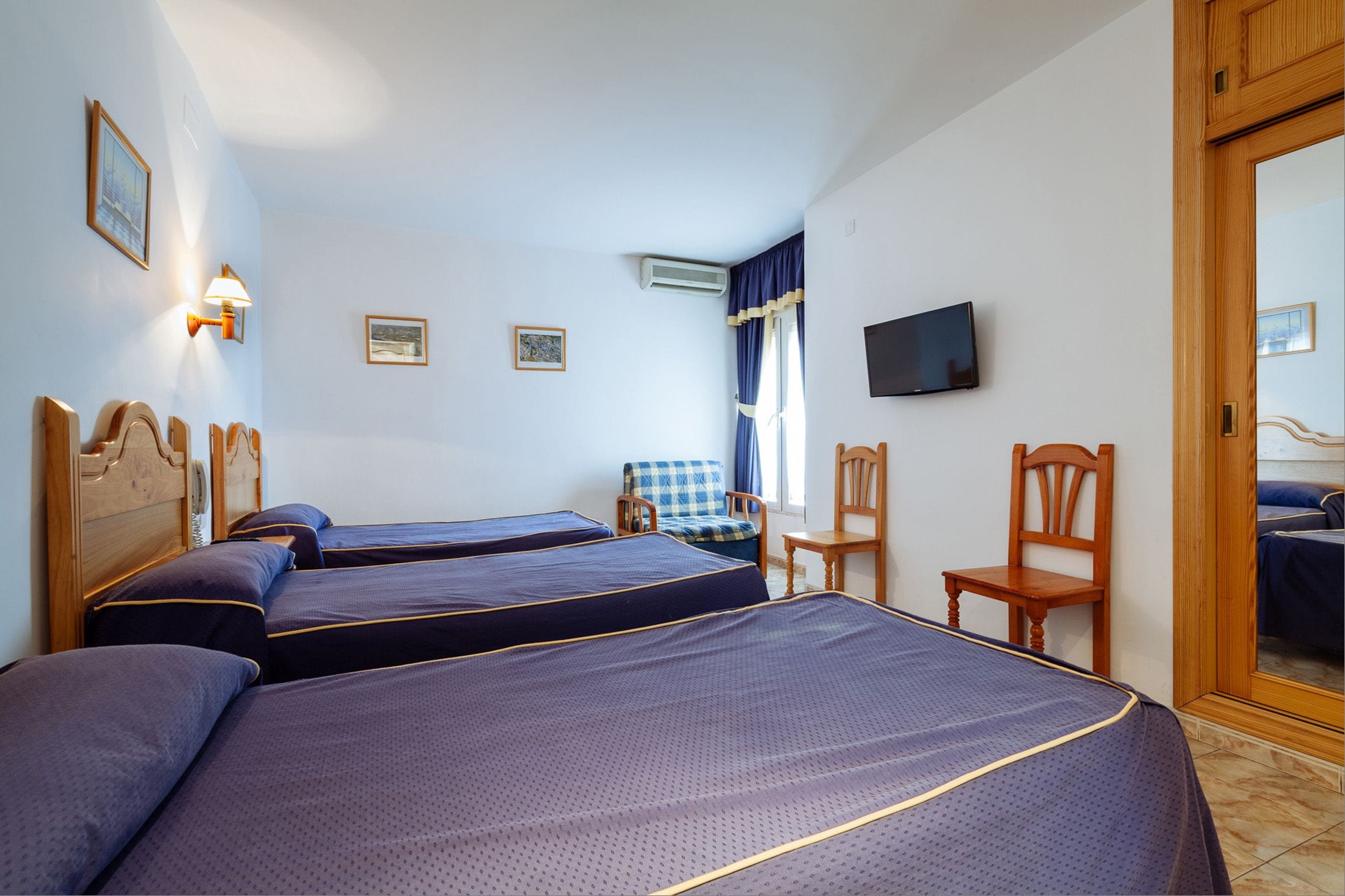 Habitación de hotel con tres camas, televisión, una silla y un escritorio.