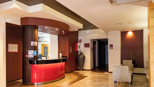 A reception area with a curved red counter, a large vase, and a seating area with chairs. - Hotel Philadelfia (Peligros)