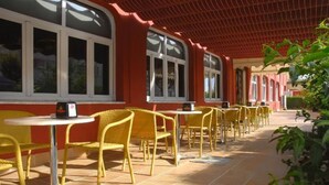 An outdoor cafe with yellow wicker chairs and tables, red walls, and large windows. - Hotel Philadelfia (Peligros)