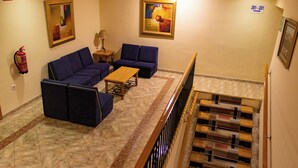 A lobby with a blue sofa set, a wooden coffee table, and a patterned carpet. There are two paintings on the walls and a fire extinguisher mounted on the wall. - Hotel Philadelfia (Peligros)