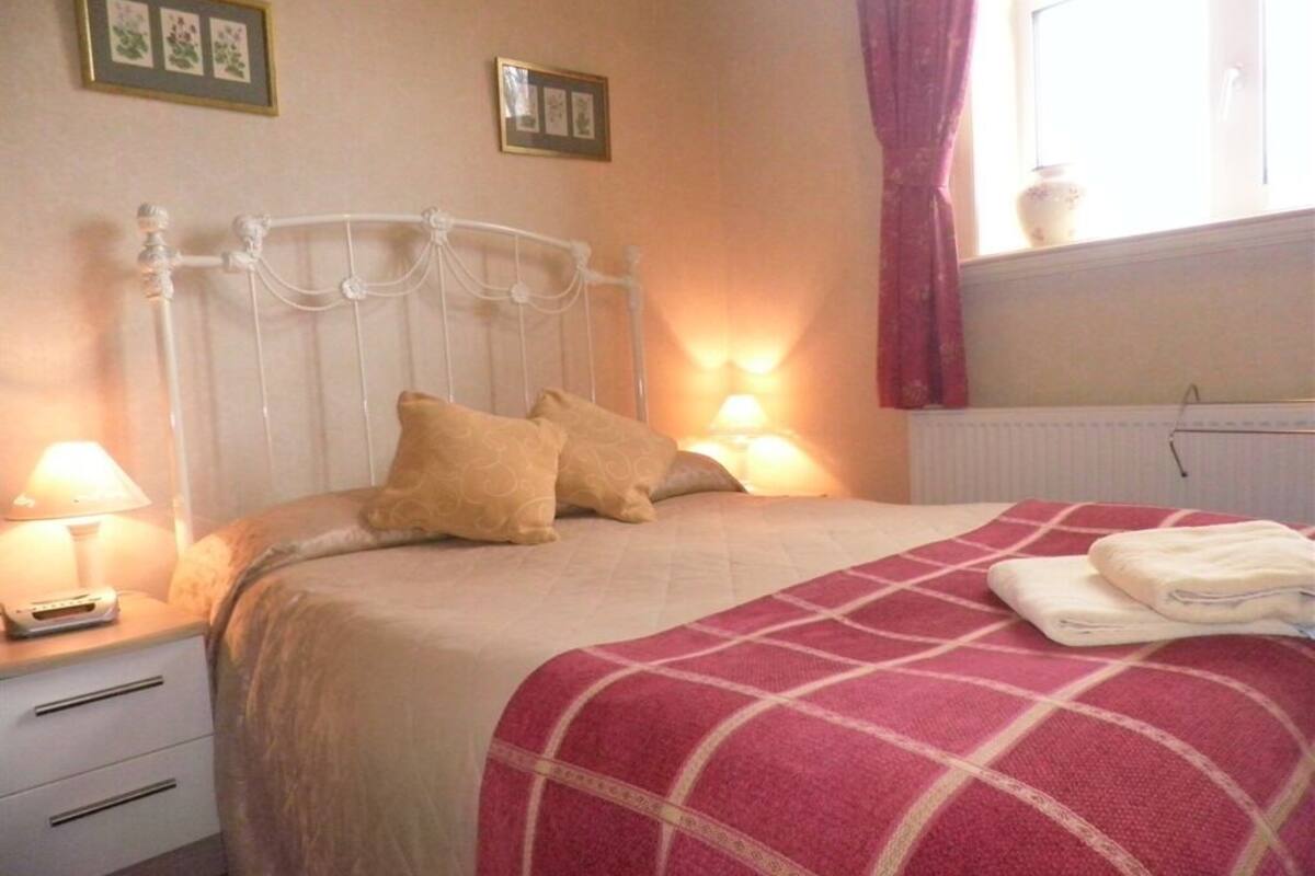 A neatly made bed with a red and white checkered blanket, a white headboard, and two bedside lamps.