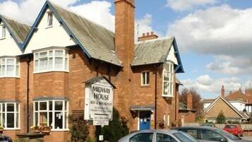 Un edificio de dos pisos con un cartel que dice 'Midway House', ofreciendo hospedaje y desayuno.