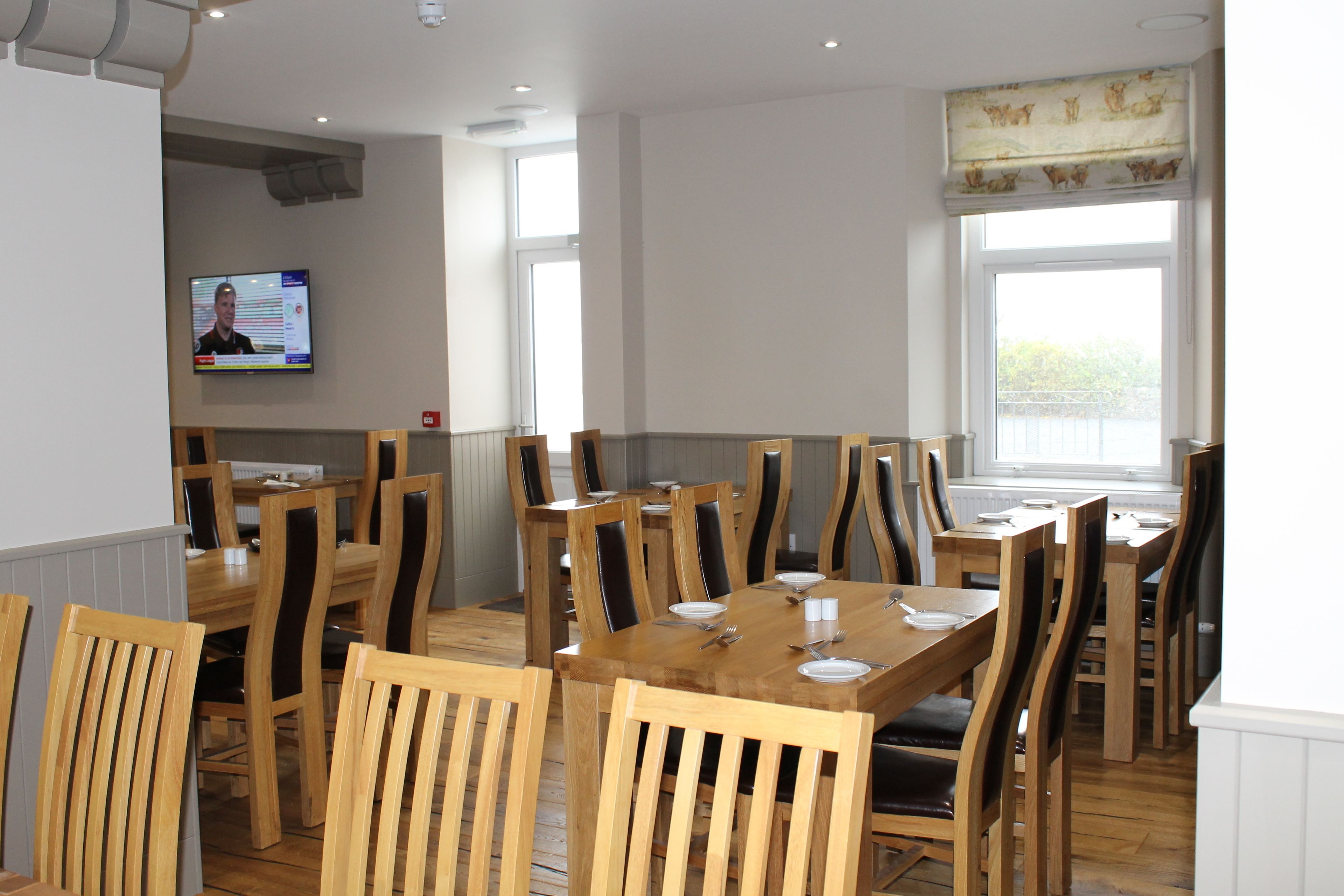 A dining area with wooden tables and chairs, a television screen, and a window with a view.