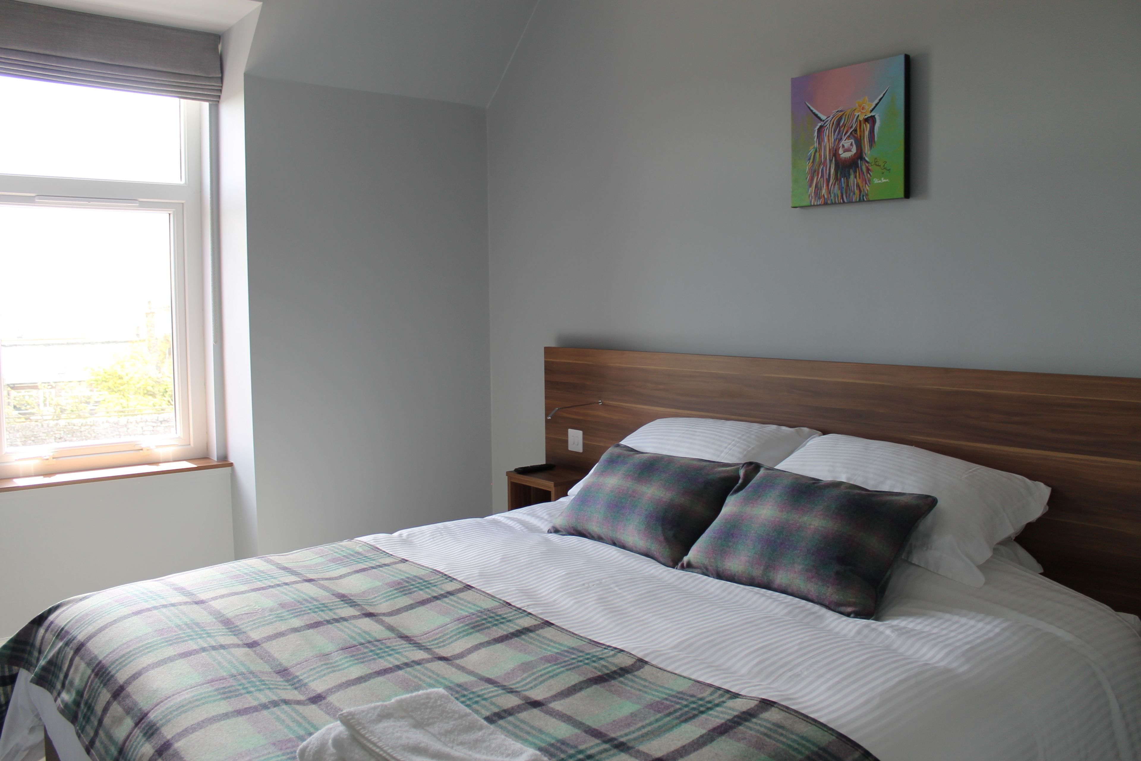A neatly made bed with a plaid bedspread, a wooden headboard, and a painting on the wall.