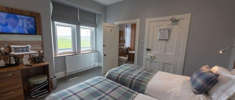 A hotel room with two beds, a desk, a television, and a bathroom visible through an open door.