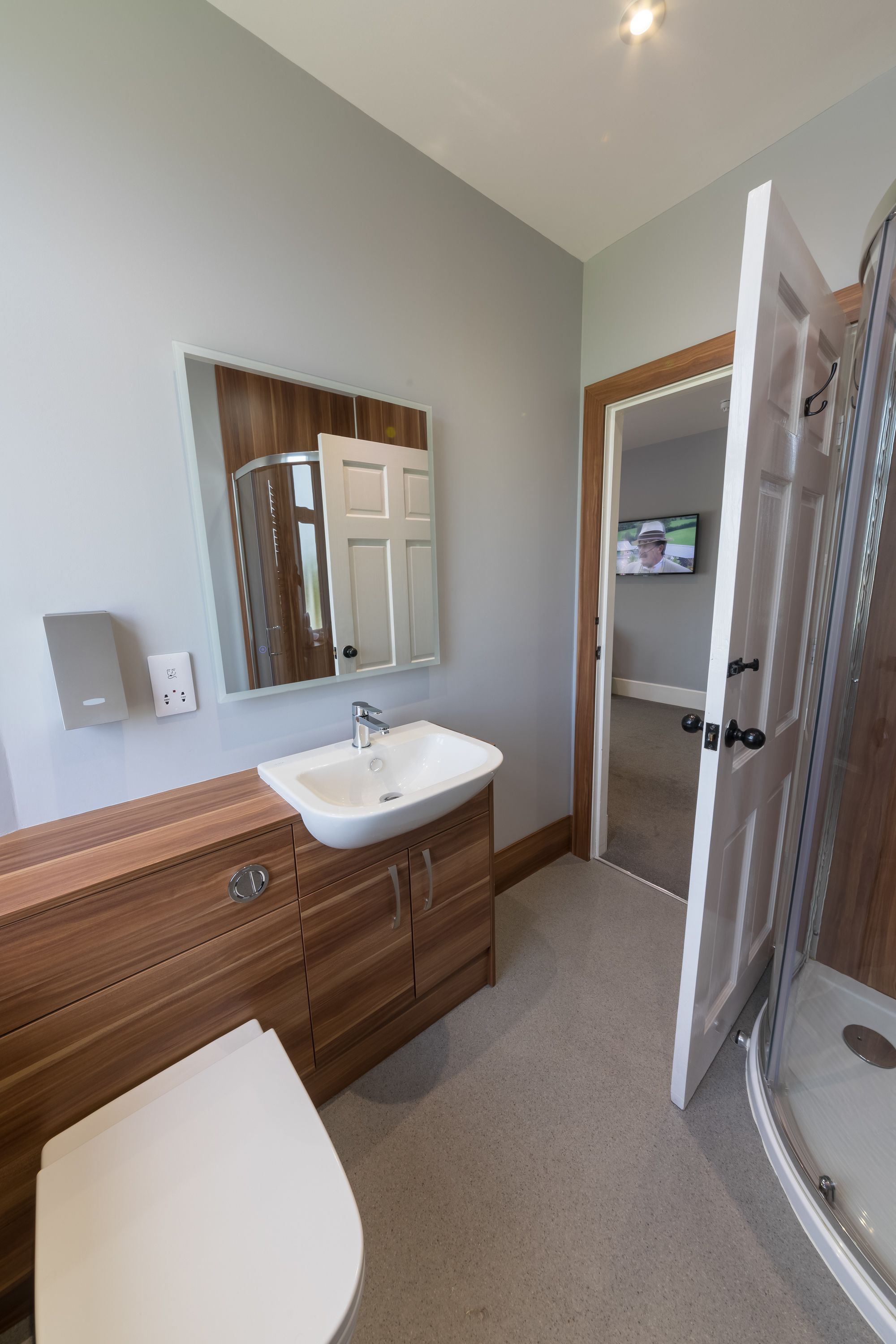 A bathroom with a white sink, wooden vanity, and a shower area.