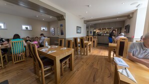 Un restaurant avec des tables et des chaises en bois, un coin bar et des œuvres d’art encadrées accrochées aux murs.