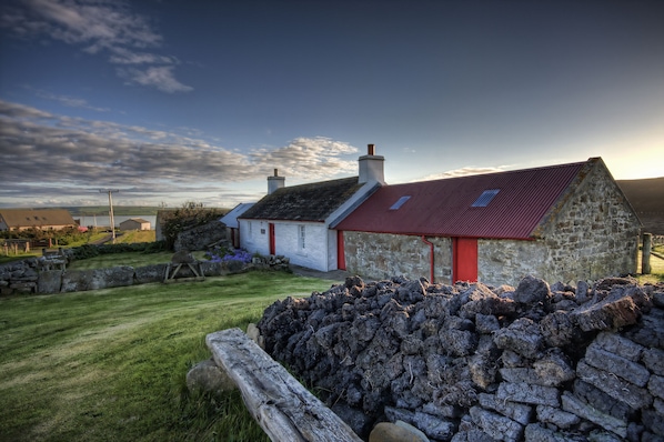 A stone house with a red roof and a small garden area.