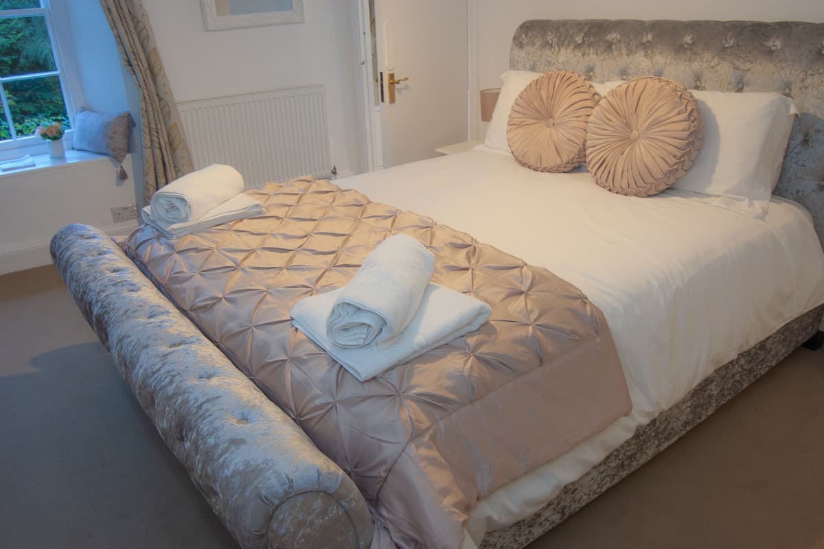 A neatly made bed with a quilted headboard, rolled white towels, and two decorative pillows.