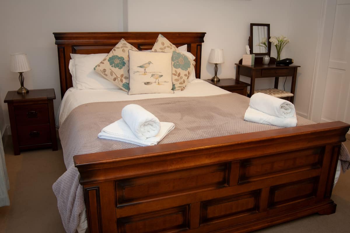 A neatly made bed with floral pillows, a wooden headboard, and two bedside tables with lamps.